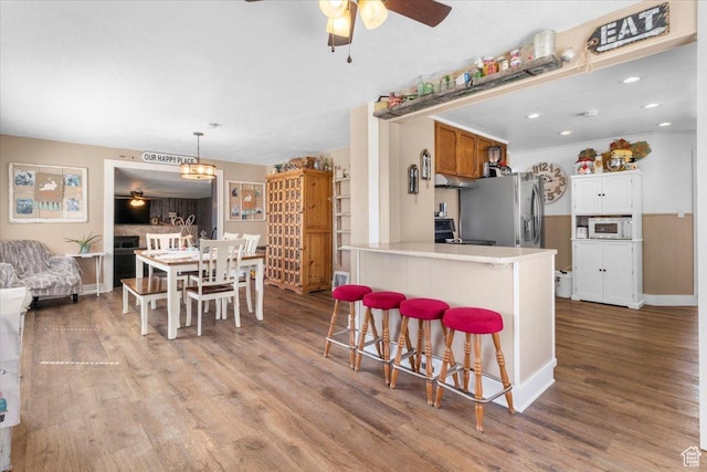 kitchen featuring stainless steel fridge with ice dispenser, a breakfast bar, ceiling fan, white microwave, and wood finished floors