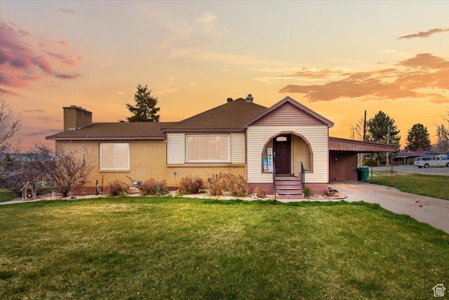 view of front of property with a chimney, concrete driveway, brick siding, a front lawn, and a carport