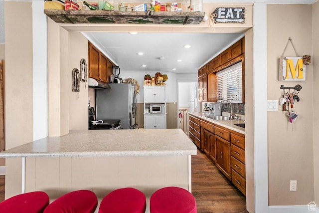 kitchen featuring light countertops, a sink, a peninsula, brown cabinetry, and dark wood-style flooring
