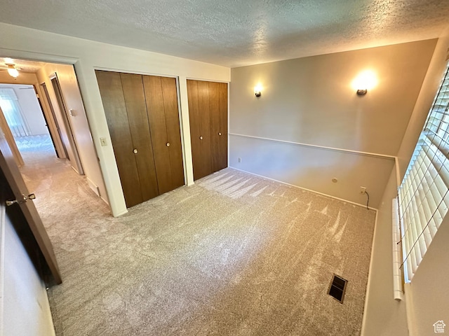 unfurnished bedroom featuring a textured ceiling, multiple closets, carpet, and multiple windows