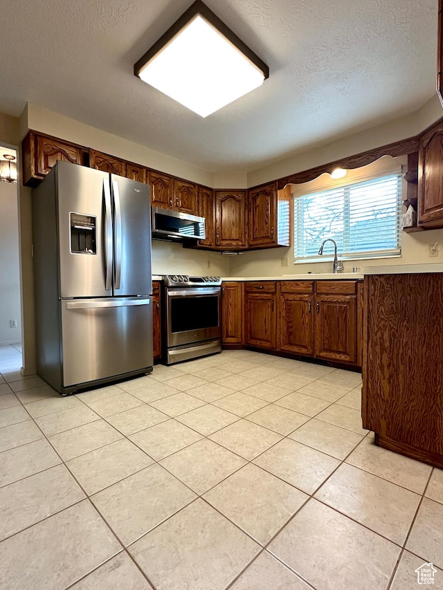 kitchen with stainless steel appliances, a sink, a textured ceiling, light countertops, and light tile patterned flooring