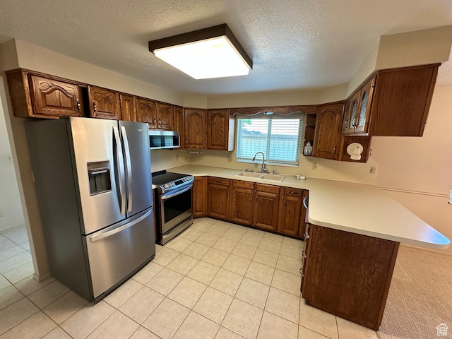 kitchen with appliances with stainless steel finishes, a peninsula, a sink, a textured ceiling, and light countertops