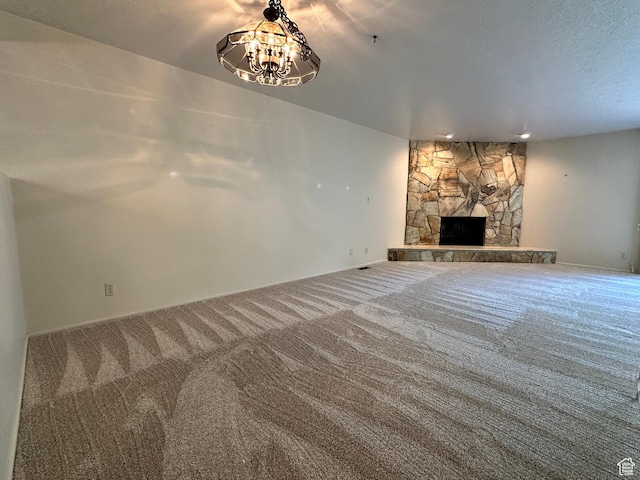 unfurnished living room featuring carpet flooring, a stone fireplace, a chandelier, and baseboards