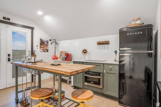 kitchen with butcher block counters, black appliances, light wood finished floors, vaulted ceiling, and green cabinets
