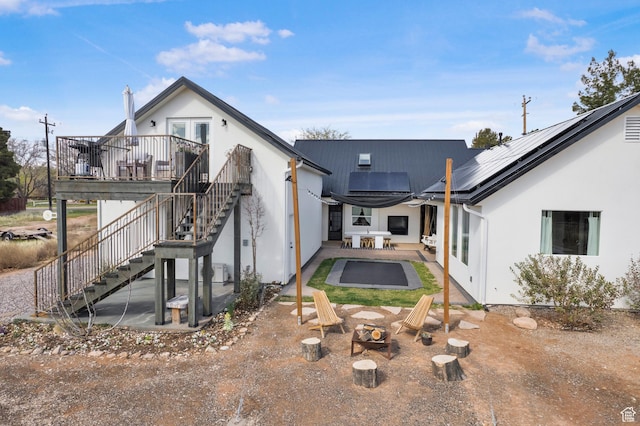 back of property featuring a patio, stucco siding, stairway, a fire pit, and roof mounted solar panels