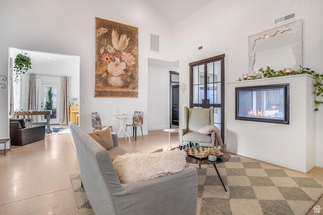 living area featuring a towering ceiling, a glass covered fireplace, and visible vents