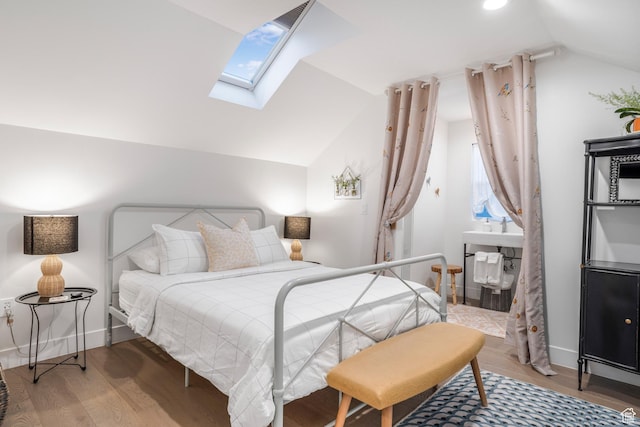 bedroom with vaulted ceiling with skylight, baseboards, and wood finished floors