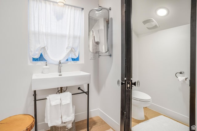 bathroom featuring visible vents, toilet, wood finished floors, a sink, and baseboards