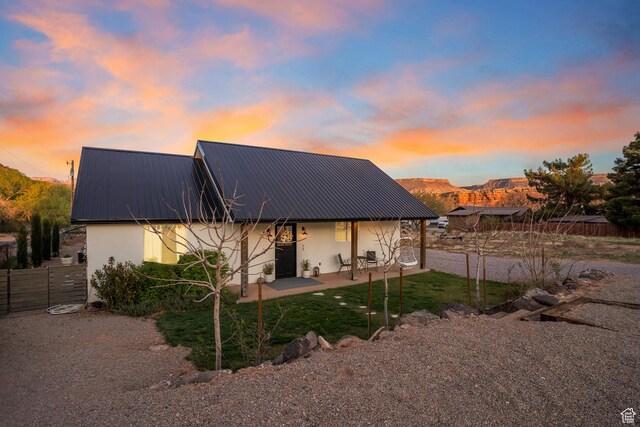 back of house at dusk with stucco siding, metal roof, a patio area, fence, and a mountain view