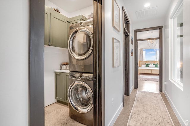 washroom featuring visible vents, baseboards, stacked washer and clothes dryer, and cabinet space
