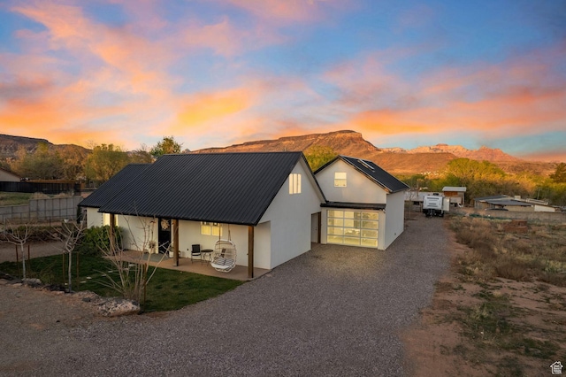 view of front of house featuring a patio, stucco siding, a mountain view, gravel driveway, and metal roof