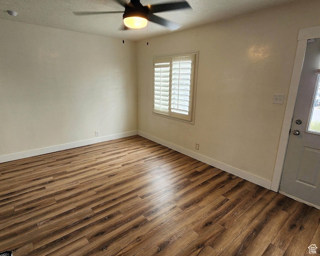 empty room featuring dark wood finished floors, baseboards, a textured ceiling, and a ceiling fan