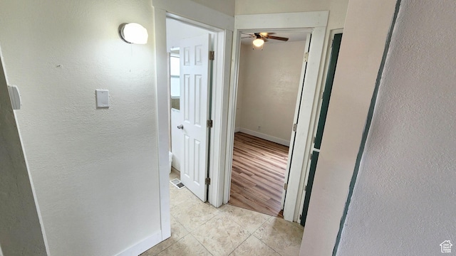 hallway with light tile patterned floors, a textured wall, and baseboards