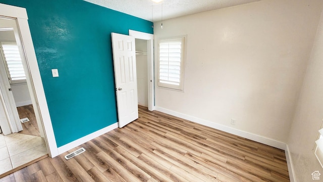 unfurnished bedroom featuring baseboards, a textured ceiling, visible vents, a closet, and wood finished floors