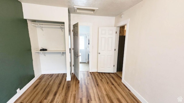 unfurnished bedroom featuring a closet, baseboards, wood finished floors, and attic access