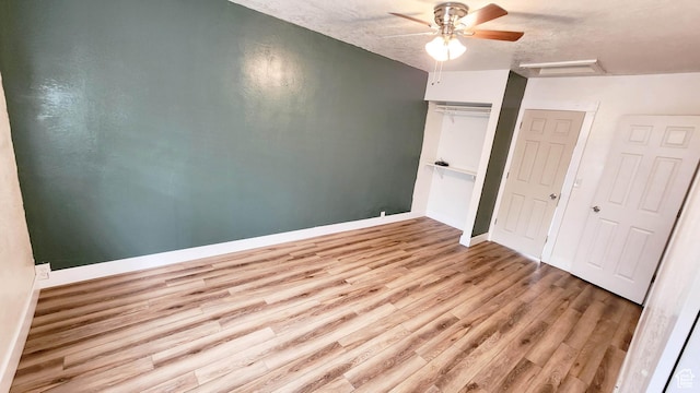 unfurnished bedroom with a textured ceiling, baseboards, ceiling fan, wood finished floors, and attic access