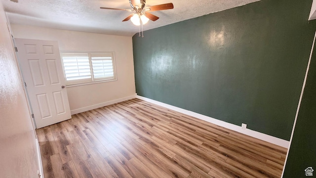 empty room with baseboards, a textured ceiling, wood finished floors, and a ceiling fan