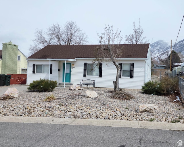 ranch-style house featuring a shingled roof, a mountain view, and fence