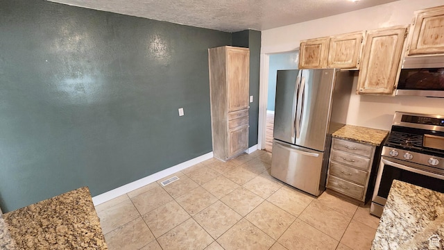 kitchen featuring baseboards, a textured ceiling, visible vents, light brown cabinets, and appliances with stainless steel finishes