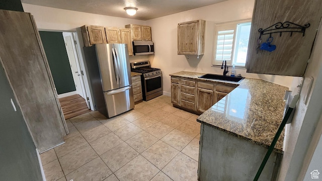 kitchen with light tile patterned floors, a sink, appliances with stainless steel finishes, and baseboards