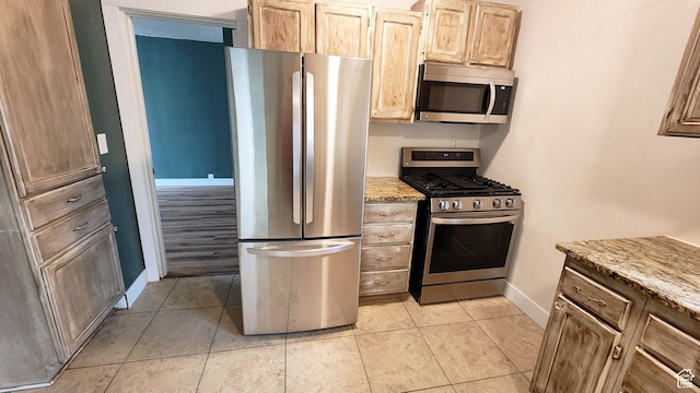 kitchen featuring light stone countertops, stainless steel appliances, baseboards, and light tile patterned flooring