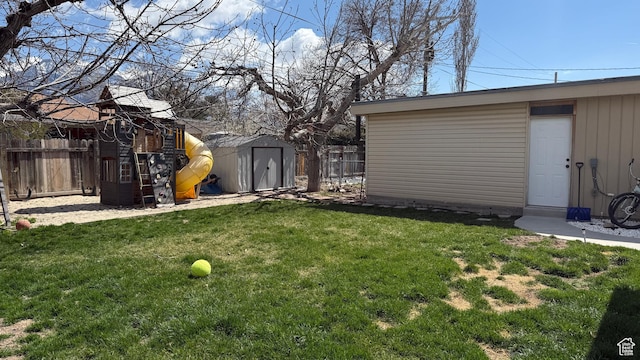 view of yard with an outdoor structure, a storage shed, fence, and a playground