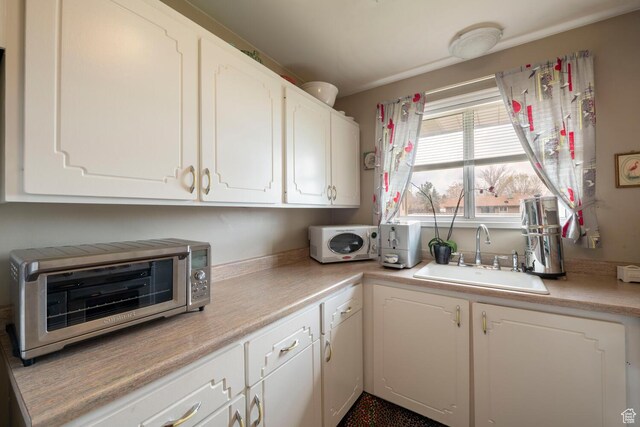 kitchen with white cabinetry, a sink, light countertops, and a toaster