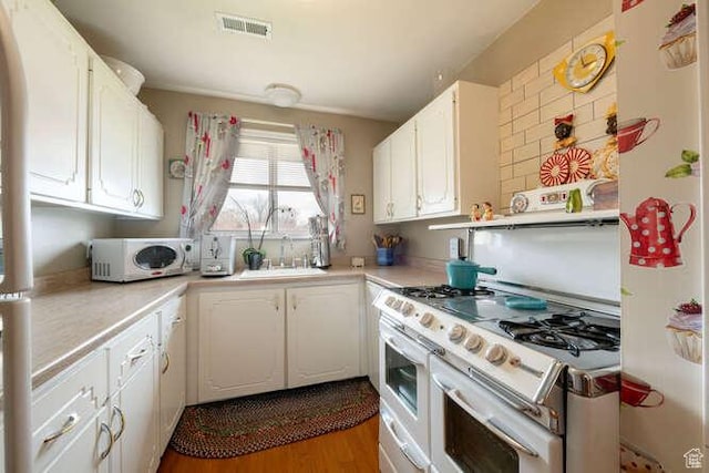 kitchen with white cabinetry, light countertops, white appliances, a sink, and visible vents