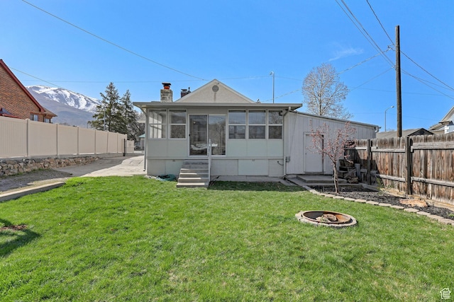 rear view of property with a yard, a fire pit, a fenced backyard, and a sunroom