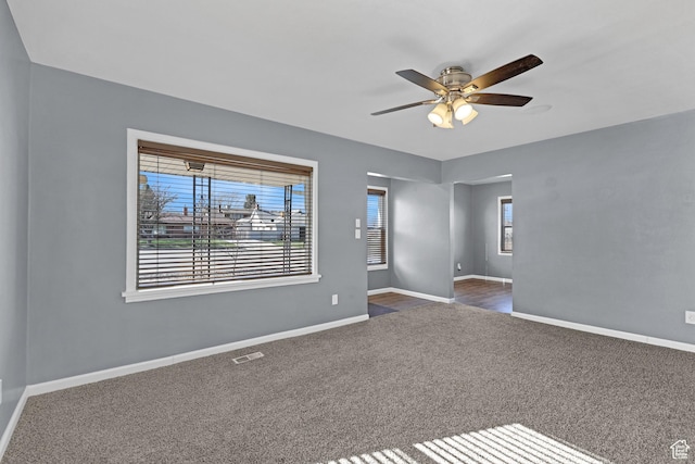 empty room featuring a wealth of natural light, visible vents, dark carpet, and ceiling fan