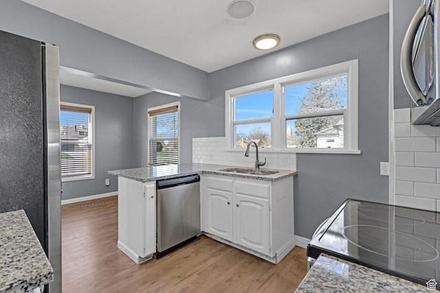 kitchen with white cabinets, a sink, appliances with stainless steel finishes, light wood-style floors, and a peninsula