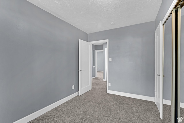 unfurnished bedroom with a textured ceiling, a closet, carpet flooring, and baseboards
