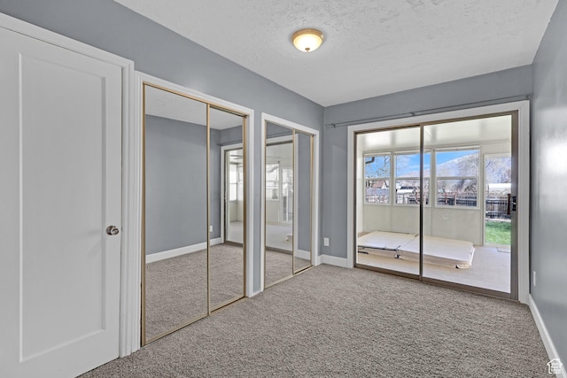 unfurnished bedroom with two closets, baseboards, a textured ceiling, and carpet floors