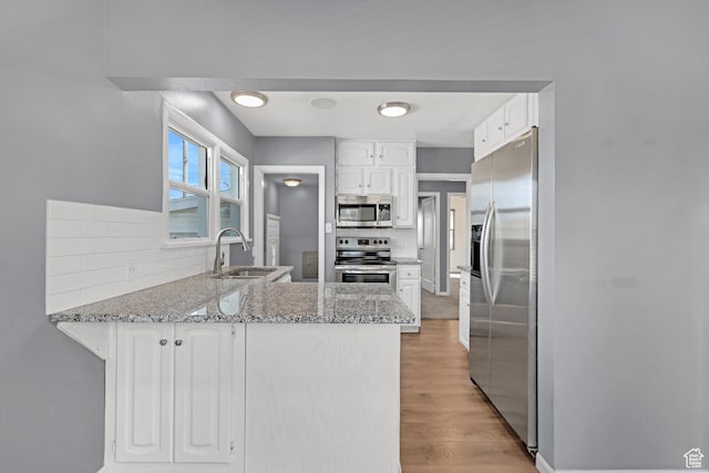 kitchen with a sink, light wood-type flooring, appliances with stainless steel finishes, a peninsula, and backsplash