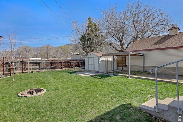 view of yard featuring a storage shed, a fenced backyard, a fire pit, and an outdoor structure