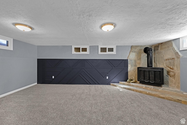 interior space featuring a textured ceiling, a wood stove, baseboards, and carpet flooring