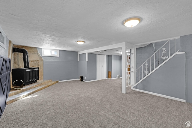 below grade area featuring a wood stove, carpet, a textured ceiling, stairway, and baseboards