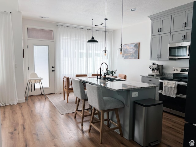 kitchen with gray cabinetry, visible vents, appliances with stainless steel finishes, a sink, and wood finished floors