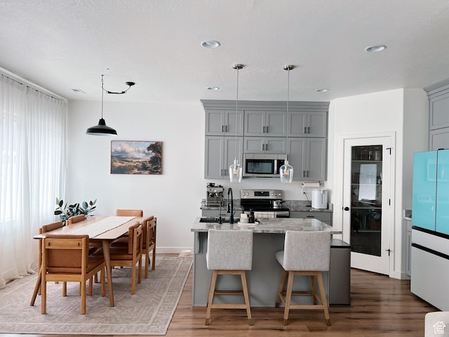 kitchen featuring appliances with stainless steel finishes, wood finished floors, a sink, hanging light fixtures, and gray cabinetry