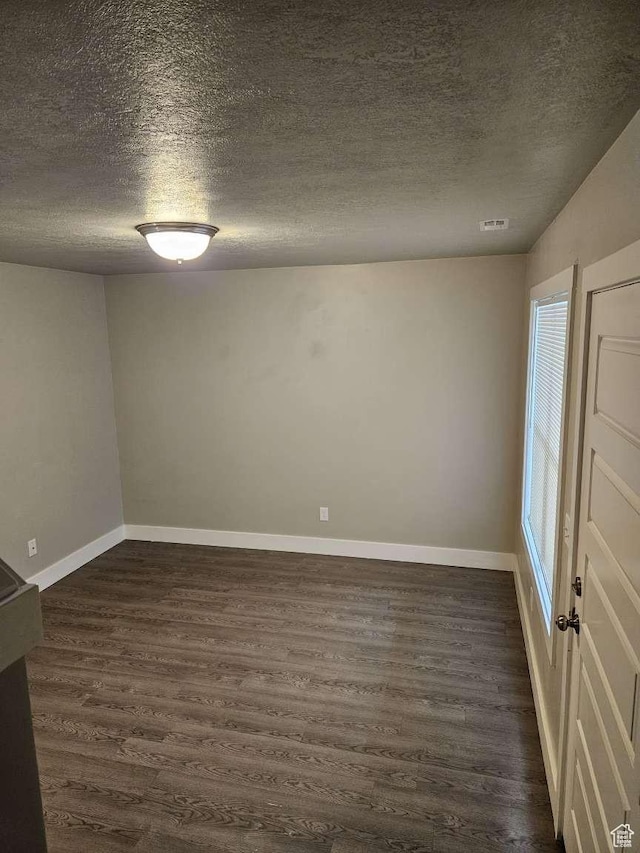 unfurnished room featuring a textured ceiling, baseboards, dark wood finished floors, and visible vents