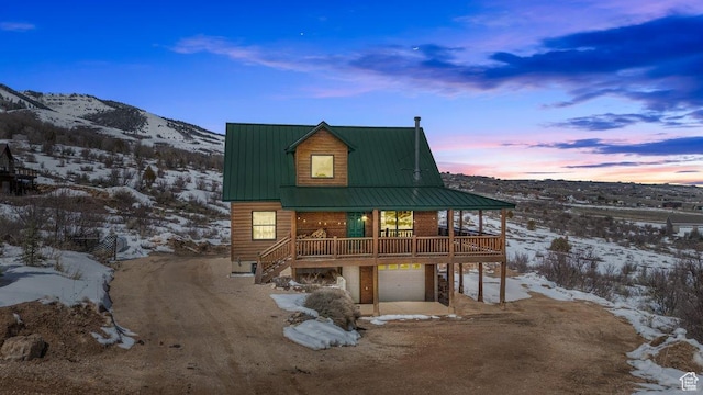 snow covered back of property with a mountain view, metal roof, a garage, stairs, and driveway