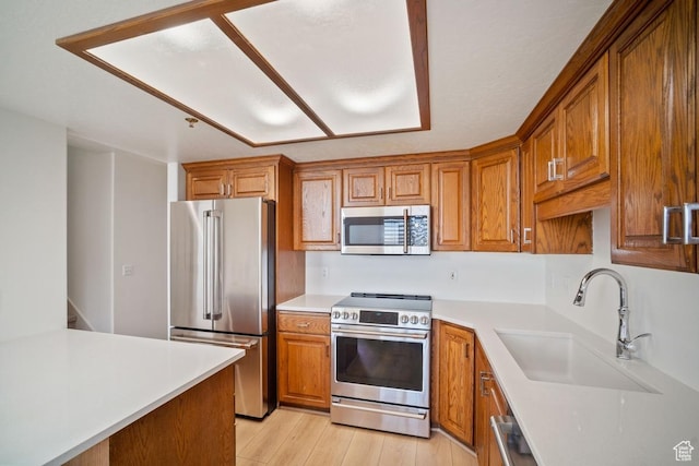 kitchen with a sink, brown cabinetry, light wood-style floors, stainless steel appliances, and light countertops