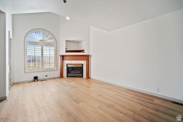 unfurnished living room with vaulted ceiling, wood finished floors, visible vents, baseboards, and a glass covered fireplace