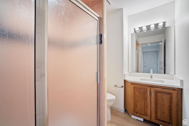 full bathroom featuring toilet, vanity, wood finished floors, and a stall shower