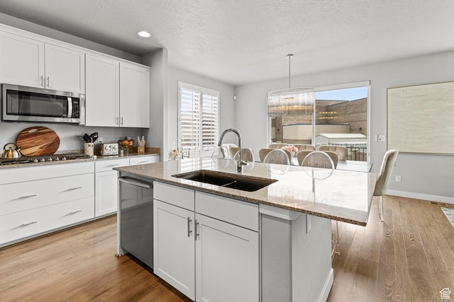 11534 S Rk Cv, South Jordan, UT 84095 - kitchen featuring stainless steel appliances, a sink, a center island with sink, light wood-style flooring, and a textured ceiling