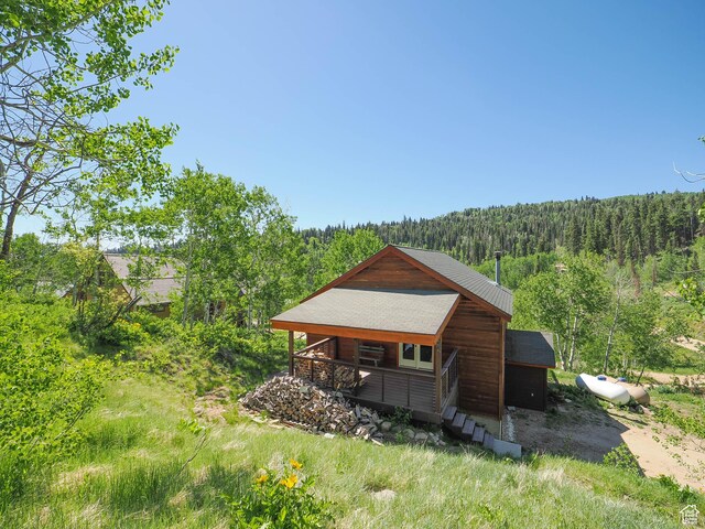 back of house with a view of trees and roof with shingles