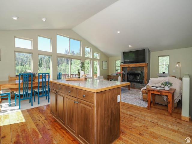 kitchen featuring a tiled fireplace, light wood-style flooring, light countertops, a kitchen island, and brown cabinets
