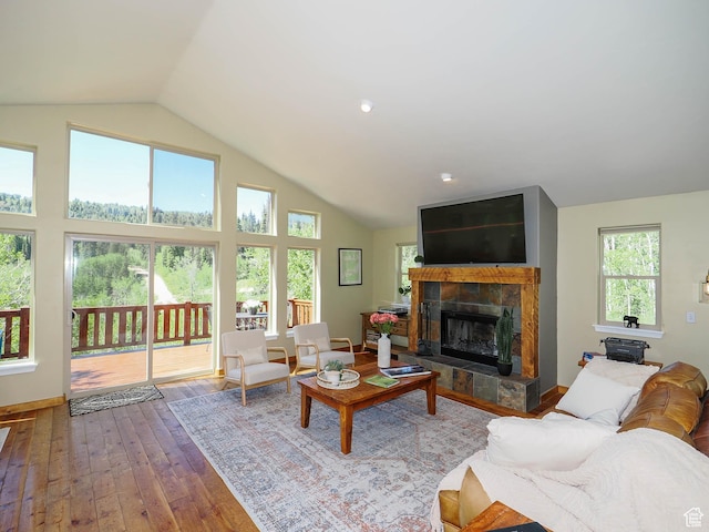 living area with a tiled fireplace, baseboards, high vaulted ceiling, and hardwood / wood-style floors
