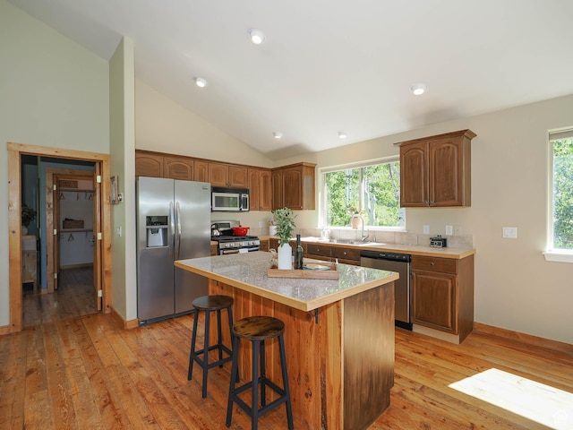 kitchen featuring light wood-type flooring, a kitchen breakfast bar, a kitchen island, stainless steel appliances, and a sink