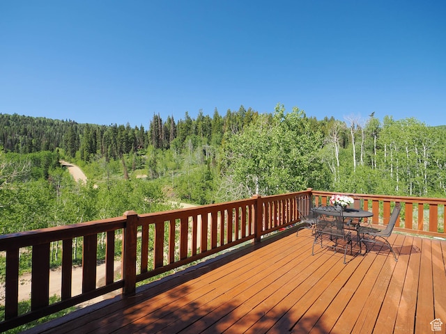 deck with a forest view and outdoor dining space